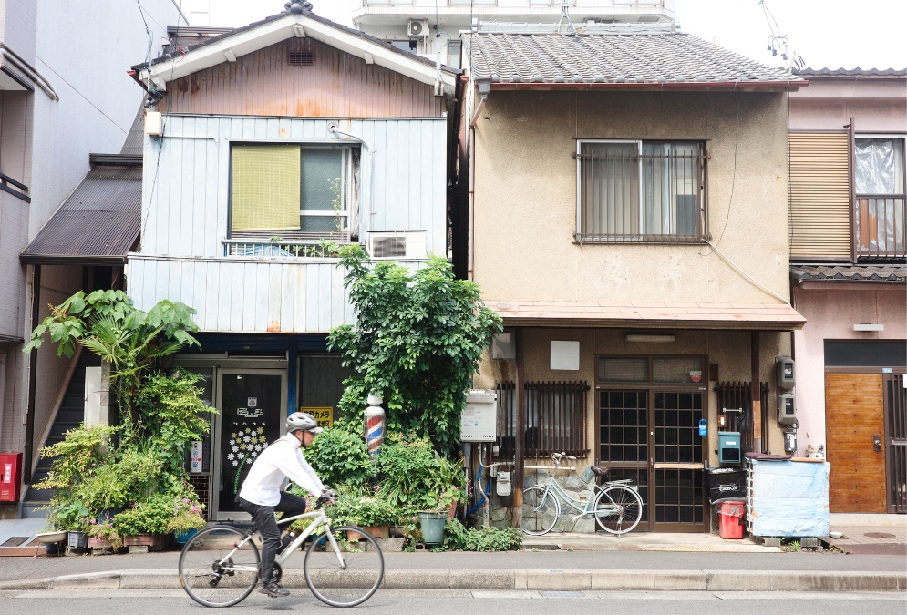 緑に囲まれた名古屋・沢上商店街の理容店前、ゆっくり自転車を走らせる人