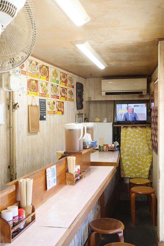 どんぶり亭の店内。壁いっぱいのメニューと細長いカウンター席が並ぶ昭和区の定食屋