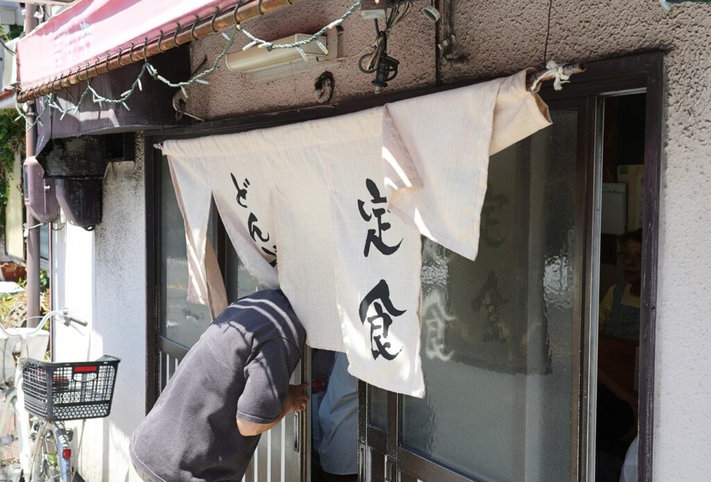 暖簾をくぐって入店する常連客。営業最終日のどんぶり亭の様子