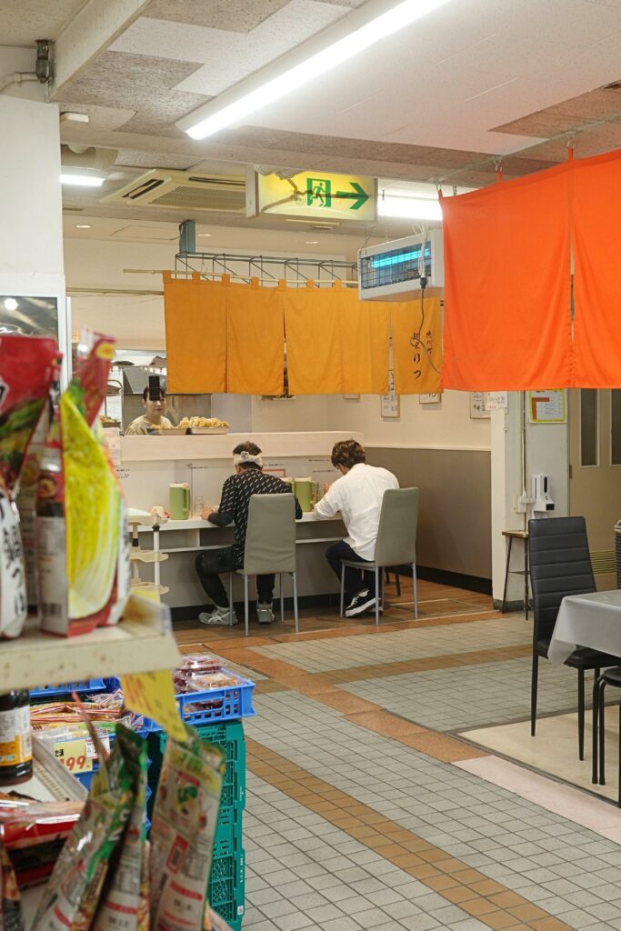 徳川公設市場の奥にある「麺家りつ」。市場の通路越しに見えるオレンジ色の暖簾と、名古屋・東区の日常風景