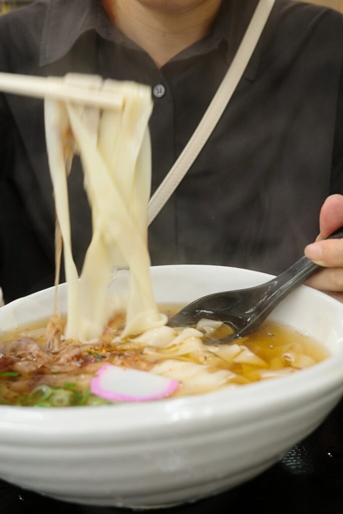 麺家りつのきしめんを持ち上げる様子。薄くひらひらとした麺と出汁の香りが伝わる一枚